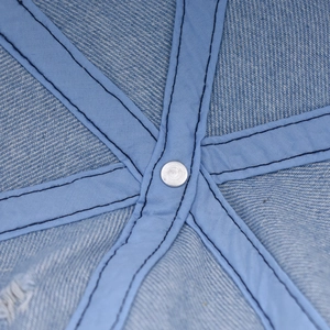 Dettaglio delle cuciture interne e del bottone metallico sul berretto in denim azzurro
