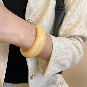 Gros plan d'un bracelet jonc épais en résine jaune porté avec une veste en tweed élégante
