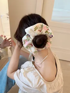 Close-up of cream satin scrunchie with detailed floral embroidery on a soft fabric texture