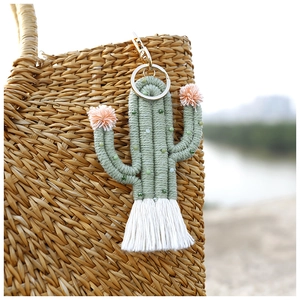 Close-up of handmade green cactus keychain with white tassels hanging on a straw bag