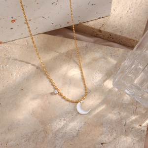 Detailed close-up of golden asymmetric chain necklace with moon pendant and zircon on stone