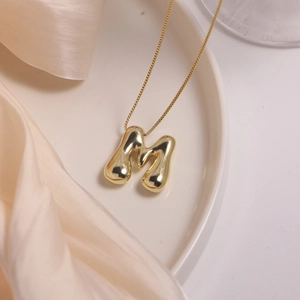 18K gold plated puff balloon letter M pendant necklace on elegant ceramic tray