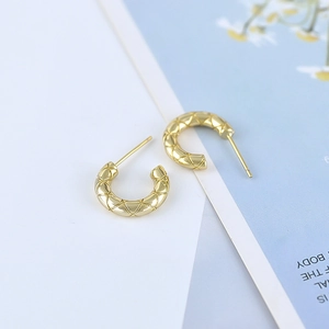 Macro shot of gold C-shaped earrings with quilted texture and polished metal finish