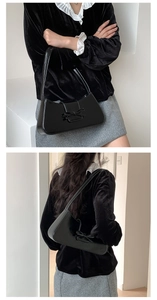 Close-up of black glossy baguette bag with bow detail worn as an underarm shoulder bag
