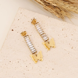 Detail of gold butterfly drop earrings with rectangular crystals on a stone background