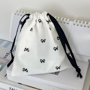 Close-up of white canvas drawstring bag with black bow print on vintage books