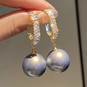 Macro shot of gold C-shaped earrings with zircon rows and a hanging blue-grey pearl