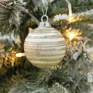 White Christmas ball with gold glitter stripes hanging on a tree with warm bokeh lights