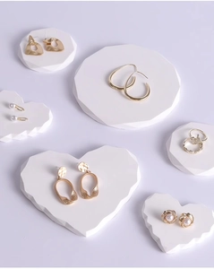 Collection of golden geometric earrings and pearl rings on white plaster jewelry stands