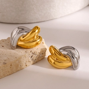 Macro view of gold and silver interlaced metal earrings on natural stone surface