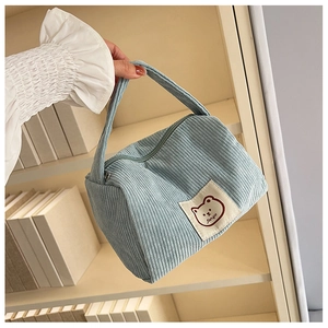 Detail of light blue corduroy handbag with cute bear patch against a bookshelf background