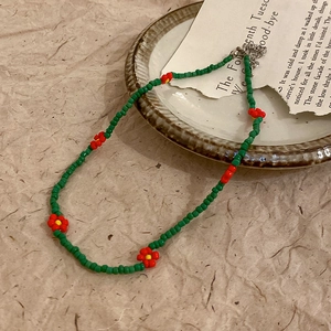 Detail of green seed bead necklace with woven floral accents on a vintage ceramic plate