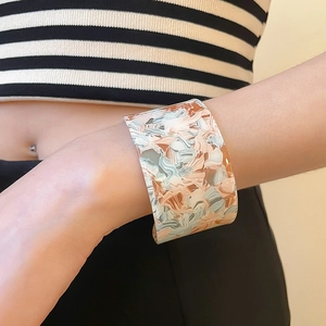 Detail of wide acrylic cuff bracelet with abstract cream and brown patterns on wrist