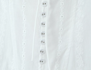 Close-up of white dress with hollow embroidery patterns and silver metal buttons