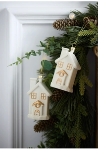 Detail view of two white ceramic house ornaments with gold trim hanging on a pine wreath