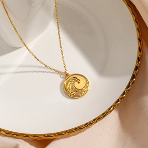 Detailed view of an 18K gold plated ocean wave relief coin pendant on a white ceramic tray