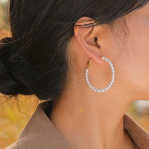 Close-up of elegant C-shaped gold hoop earrings with white pearls worn by a model
