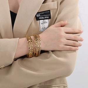 Close-up of stacked gold bangles with diamond pattern engraving on a model's wrist