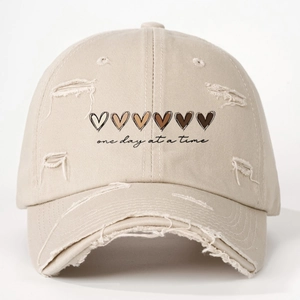 Distressed khaki baseball cap with heart icons and One Day At A Time slogan text