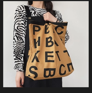 Detail of a large khaki canvas tote bag with bold black letter print and black straps