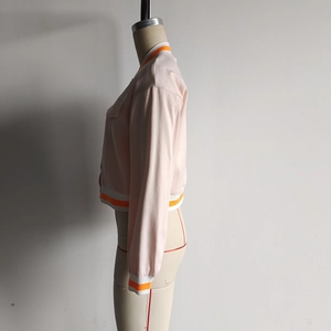 Detail of light pink cropped baseball jacket showing orange and white striped ribbed cuffs