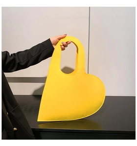Detail of a vibrant yellow heart-shaped felt handbag with a minimalist cutout handle