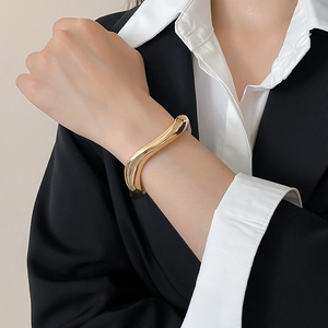 Detailed view of a wavy gold-toned metallic bracelet worn with professional business attire