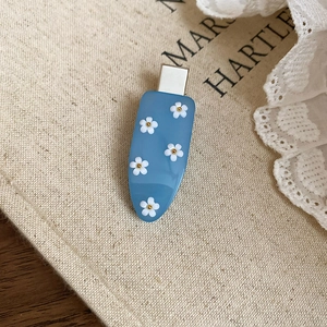 Detail of light blue hair clip featuring five white flowers with golden beads on linen