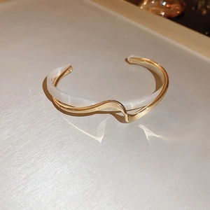 Detail of wavy gold-plated open bracelet with white resin inlay and minimalist design