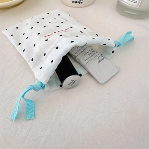 Detailed view of white polka dot drawstring pouch storing cosmetics and lipstick