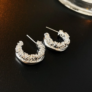 Macro shot of silver C-shaped earrings with irregular layered woven metal texture