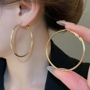Detailed view of large golden hoop earring with a sleek metallic finish worn by model