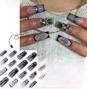 Macro detail of square press-on nails with black ombre, silver bow, and metallic cross