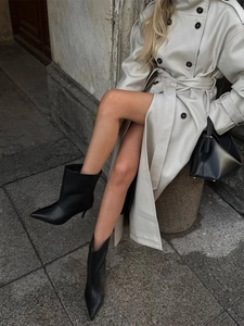 Detail of elegant black pointed-toe leather high-heel boots with a trench coat