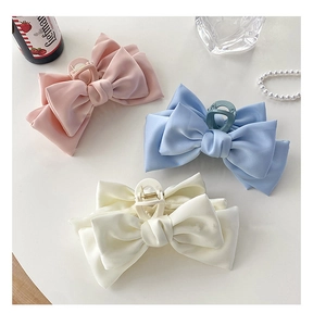 Macro detail of oversized satin bow hair claws in pink, blue and cream white