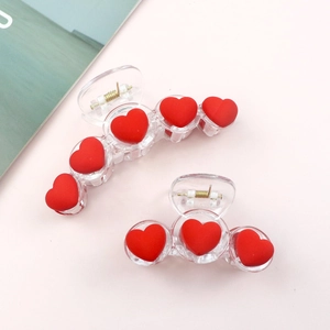 Detail shot of two transparent hair clips with red hearts on a soft pink background