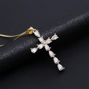 Macro d'un pendentif croix plaqué or avec zircons en forme de poire sur une chaîne fine