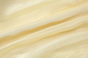 Detailed close-up of light yellow sheer fabric with soft texture and delicate pleats