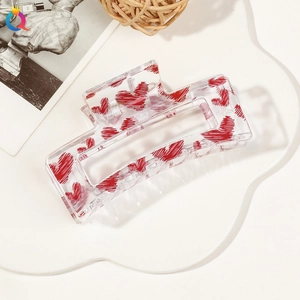 Macro shot of a clear square hair claw clip with red heart patterns on a white tray