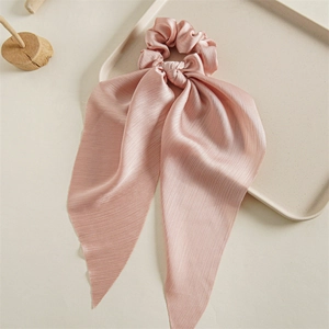 Close-up of pink satin scrunchie with long ribbons on a minimalist wood display