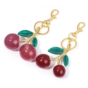 Detailed view of glitter resin cherry keychains in purple and red with gold hardware