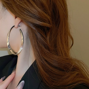 Close-up of a model wearing large silver oval hoop earrings with a flat metallic finish