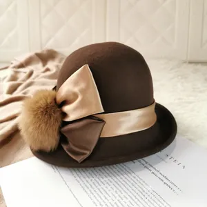 Detail of a brown wool cloche hat with champagne satin bow and decorative fur pompom