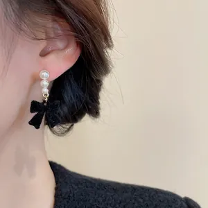 Close-up of pearl bow drop earrings featuring black velvet and golden accents