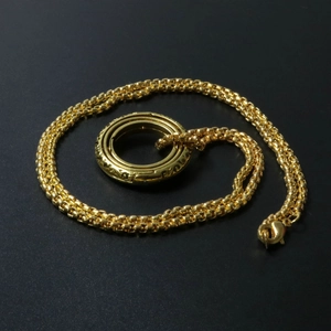 Makroaufnahme des goldenen Astronomie-Kugelrings mit Spiralkette auf strukturiertem Grund