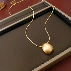 Détail du pendentif ovale plaqué or et de la chaîne serpent sur un plateau à bijoux