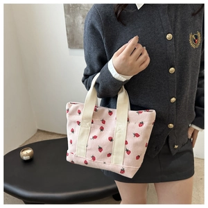 Detailed shot of a pink corduroy mini tote bag with red strawberry prints on a model