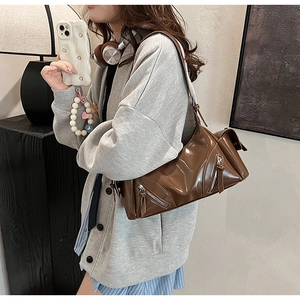Brown glossy leather shoulder bag shown on model featuring retro large capacity design