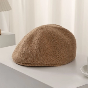 Detail of camel wool knit beret with sparkling gold thread on white platform