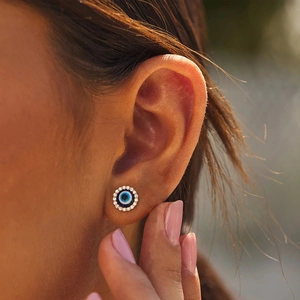 Close-up of a gold Evil Eye stud earring with blue center and crystals on a model